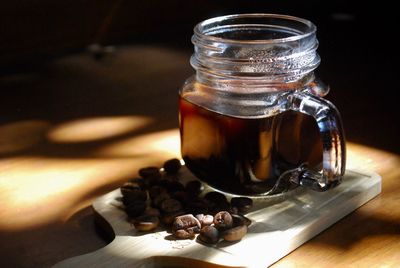 Close-up of drink by roasted coffee beans in jar on cutting board over table