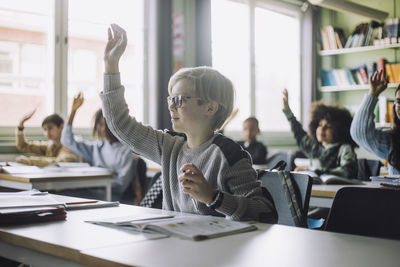 Boy with hand raised attending lecture in classroom