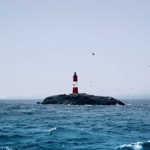 Lighthouse by sea against clear sky