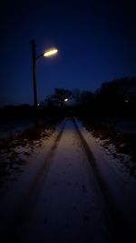 Illuminated road amidst snow against sky at night