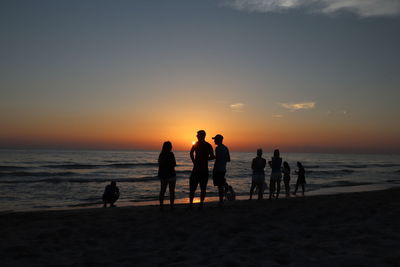 Silhouette people on beach against sky during sunset