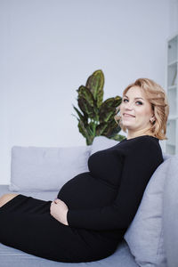 Pregnant woman in black dress smiling touching tummy