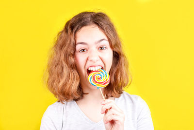 Portrait of cute girl holding lollipop against yellow background