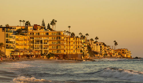 Buildings by sea against clear sky during sunset