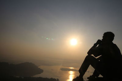 Silhouette man looking at sea against sky during sunset