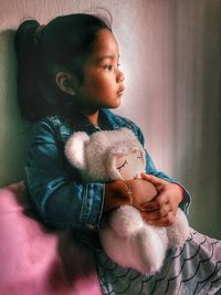 Thoughtful girl with stuffed toy sitting on bed at home