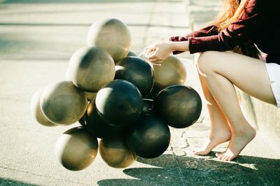 Low section of woman holding balloons while sitting on roadside