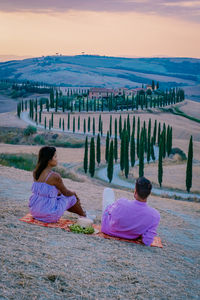 Rear view of couple sitting on land against sky during sunset