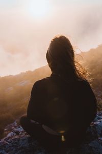 Rear view of man sitting against sky during sunset