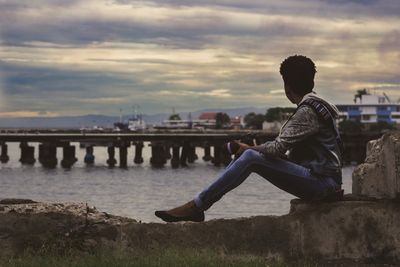 Side view of woman sitting on bridge against sky