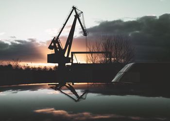 Silhouette crane by lake against sky during sunset