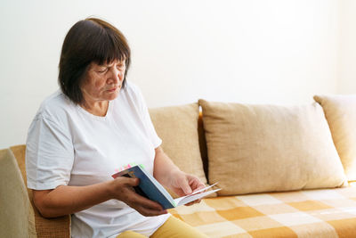 Young woman using digital tablet while sitting on bed at home