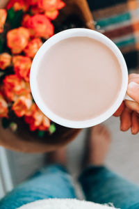 Woman holding white cup of coffee, latte cappucino, in background of bouquet orange roses flowers. 