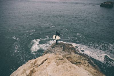 High angle view of man with surfboard standing on cliff