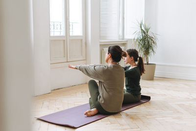 Attractive mother middle age woman and daughter teenager ptactice yoga together in the bright room