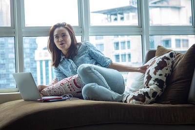 Young woman using mobile phone while sitting on sofa