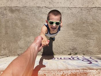 Portrait of boy holding sunglasses on wall