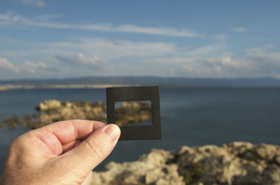 Cropped hand of person holding photographic slide against sea