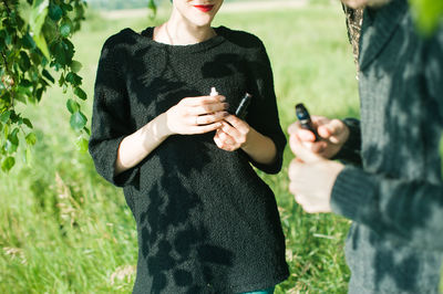 Midsection of friends with electronic cigarettes standing on field