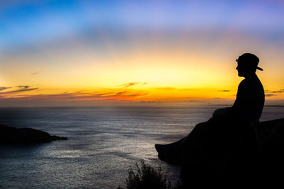 Silhouette man looking at sea against sky during sunset