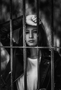 Portrait of young woman standing behind fence