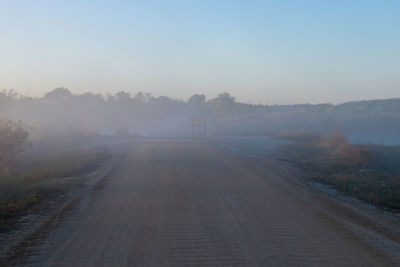 Rural dirt road leading off into the fog just after sunrise on a cool winter morning.