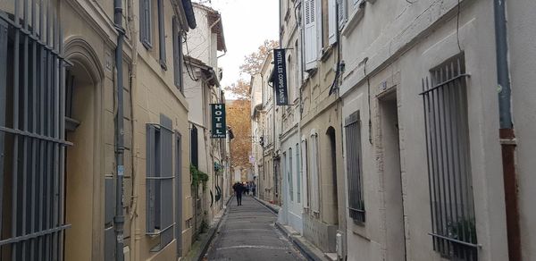 Rear view of people walking on narrow street amidst buildings