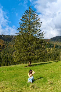 Young woman sitting in the middle of a green pasture in mountains.