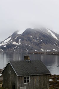 Wooden house by lake against mountain in winter