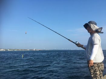 Rear view of man fishing in sea against sky