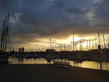 Sailboats moored at harbor against sky during sunset