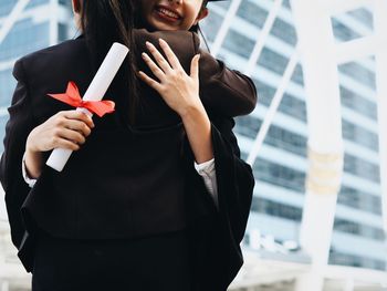 Midsection of friends embracing against building