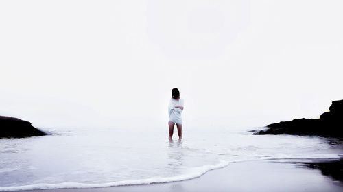 Rear view of man standing on beach against clear sky