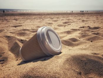 Single use cardboard and plastic coffee cup discarded on a sandy beach