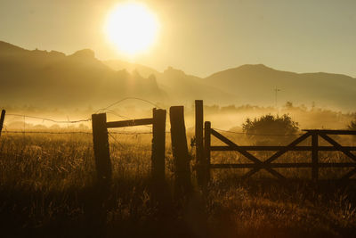 Fence on landscape against sky during sunset