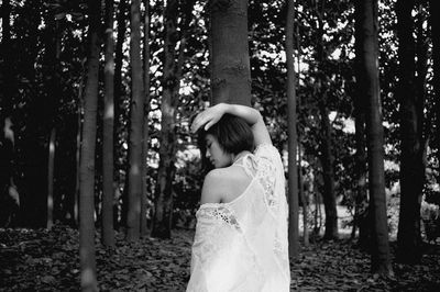 Side view of woman standing by trees in forest