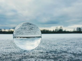 Close-up of crystal ball on frozen lake against cloudy sky