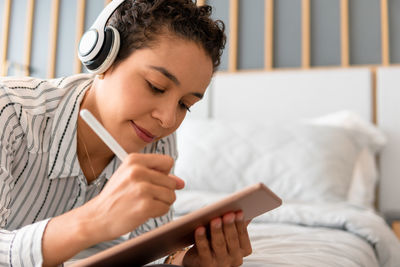 Young woman using mobile phone while sitting on bed