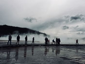 Silhouette people on wet shore against sky