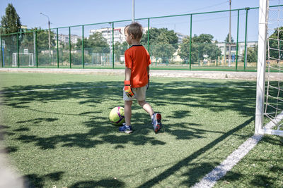 Little boy in black and orange form playing football on field, young soccer player, goalkeeper