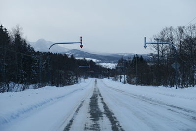 Snow covered road amidst trees against sky