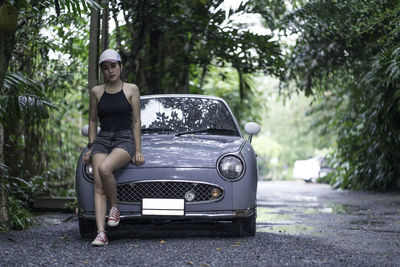 Portrait of woman leaning on car against trees