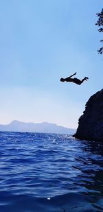 Boy jumping in sea against sky