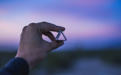Cropped hand holding triangle shape structure against sky at dusk