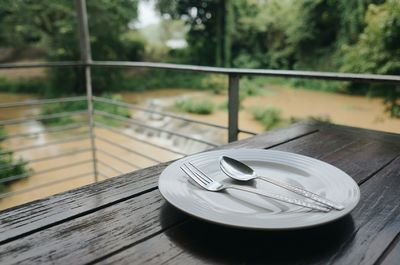 Close-up of empty plate with cutleries on wooden table in balcony