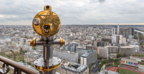 Coin-operated binocular by cityscape against sky