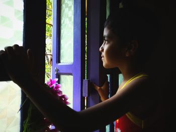 Side view portrait of a girl looking through window at home