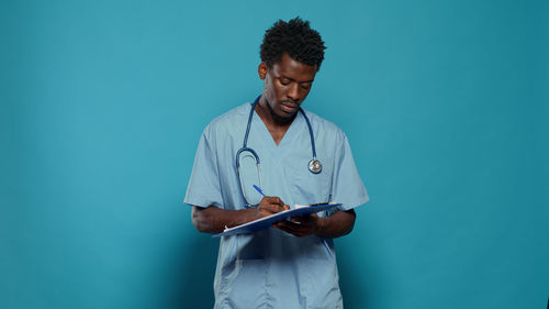 Nurse writing on notepad against blue background