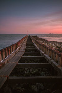 Boardwalk leading towards sea against sky during sunset