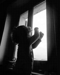 Rear view of woman looking through window at home